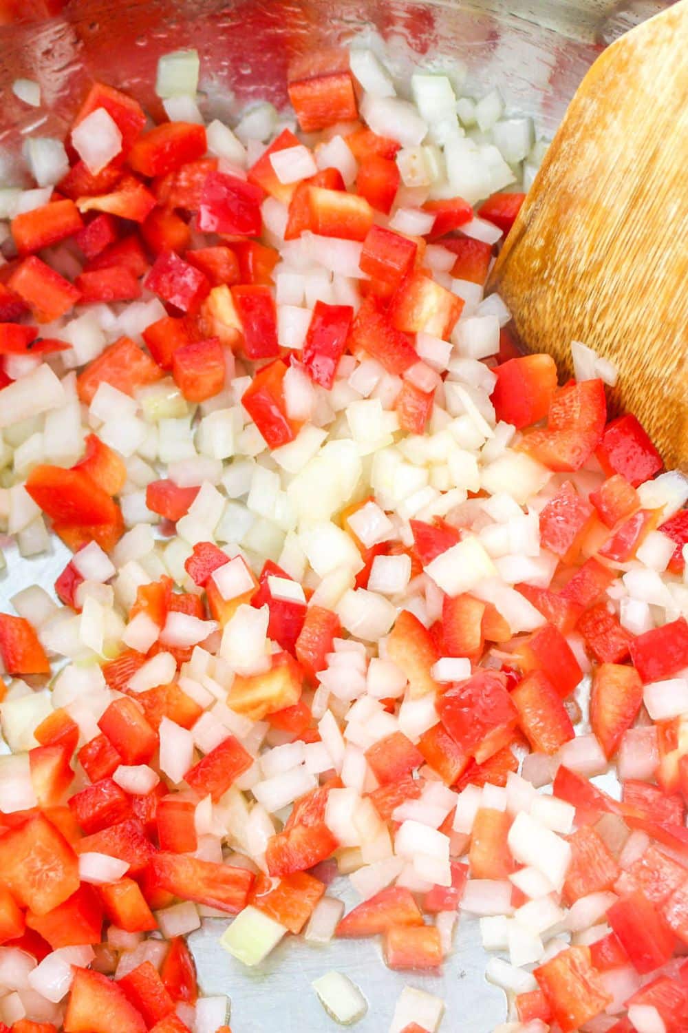 finely diced onion and red bell pepper in a skillet with a wooden spoon in the pan