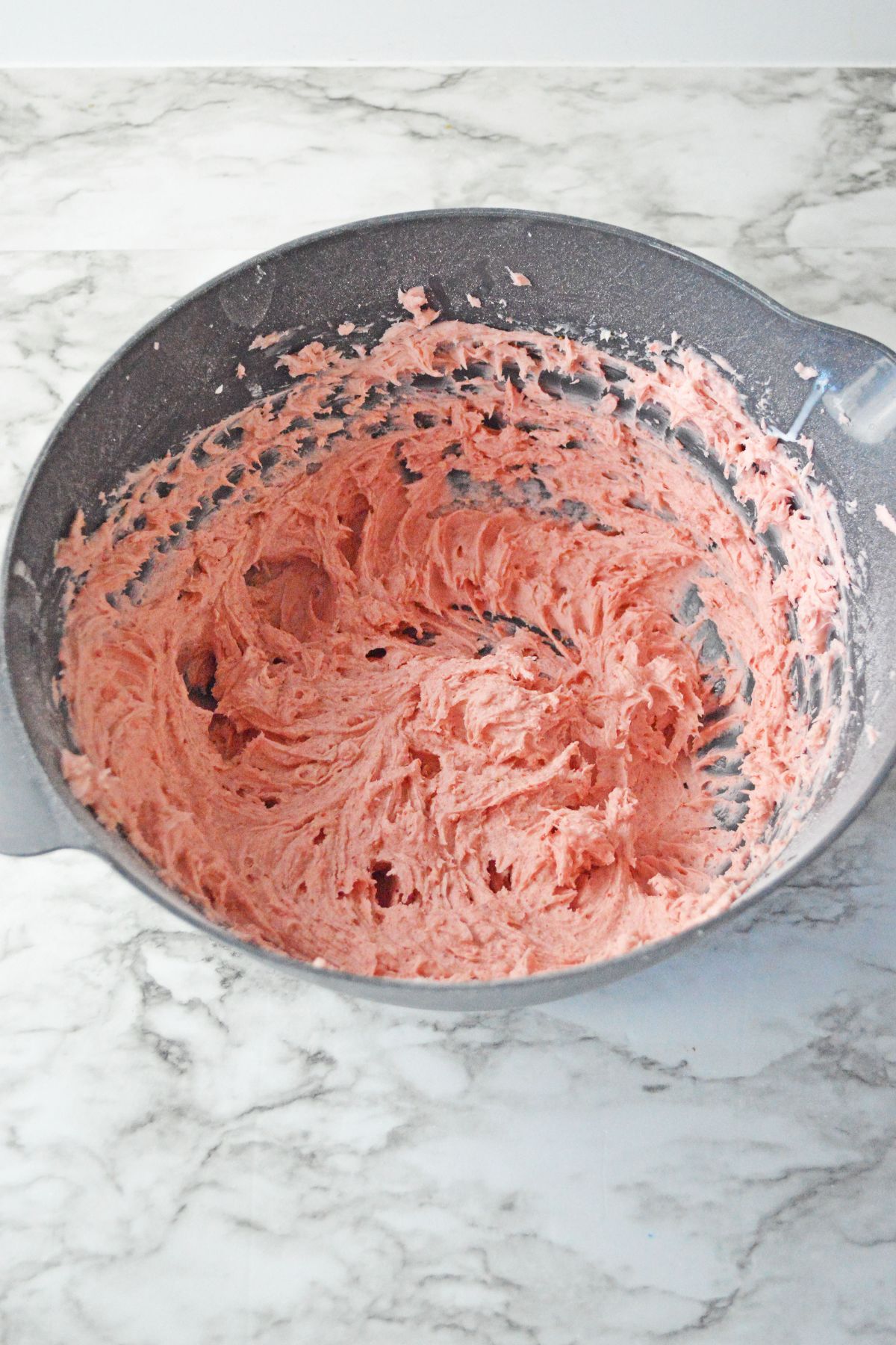 strawberry buttercream frosting being mixed in a large bowl.