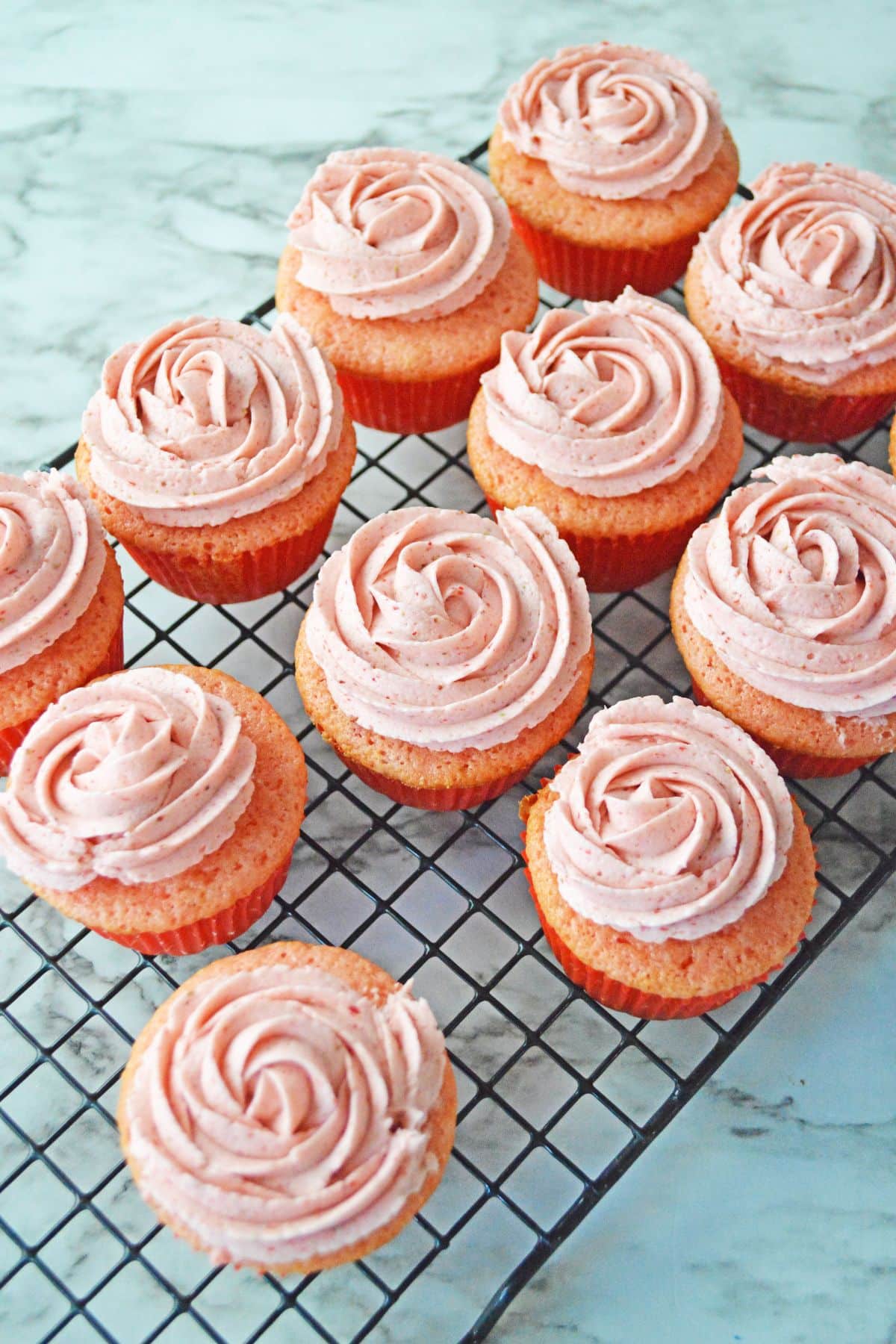 strawberry cupcakes frosting on a wire cooling rack.