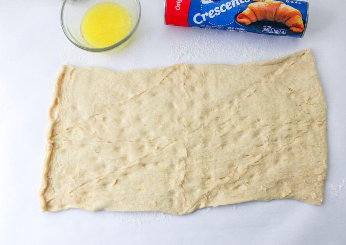 crescent roll dough being rolled out and the seams pinched together.