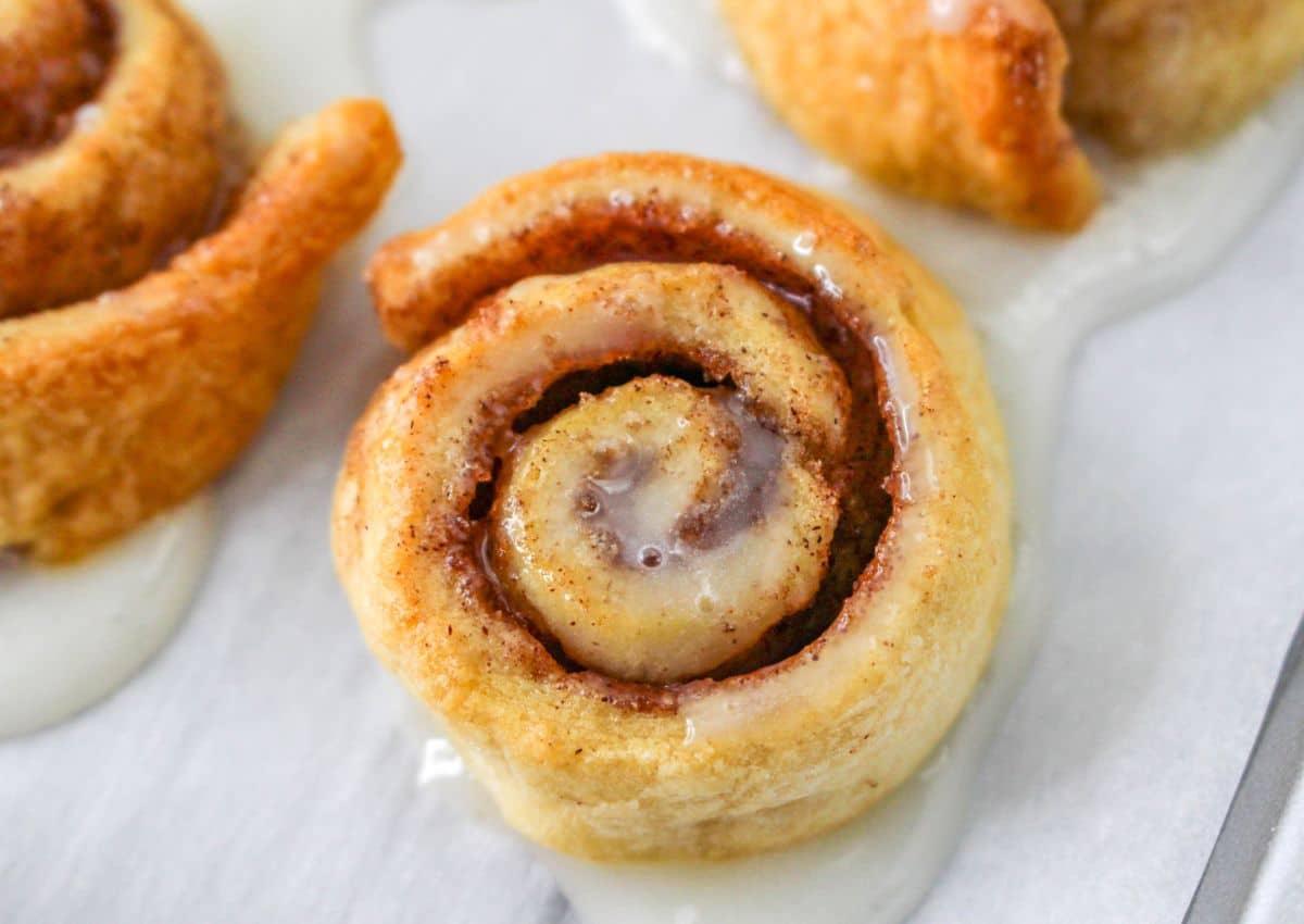 cinnamon rolls being topped with a glaze on a parchment lined baking sheet.