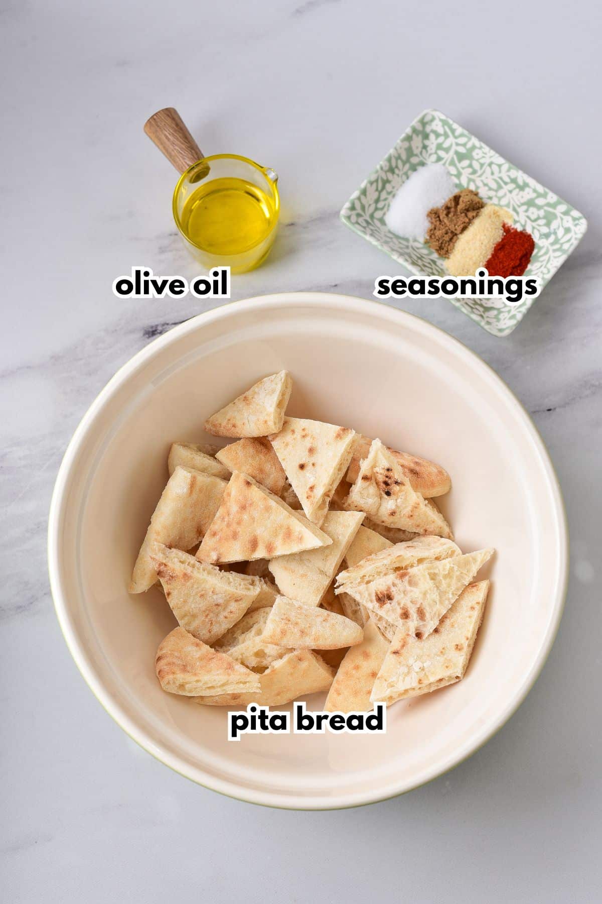 bowl of pita bread cut into triangles, cup of oil, and a small plate full of seasonings.