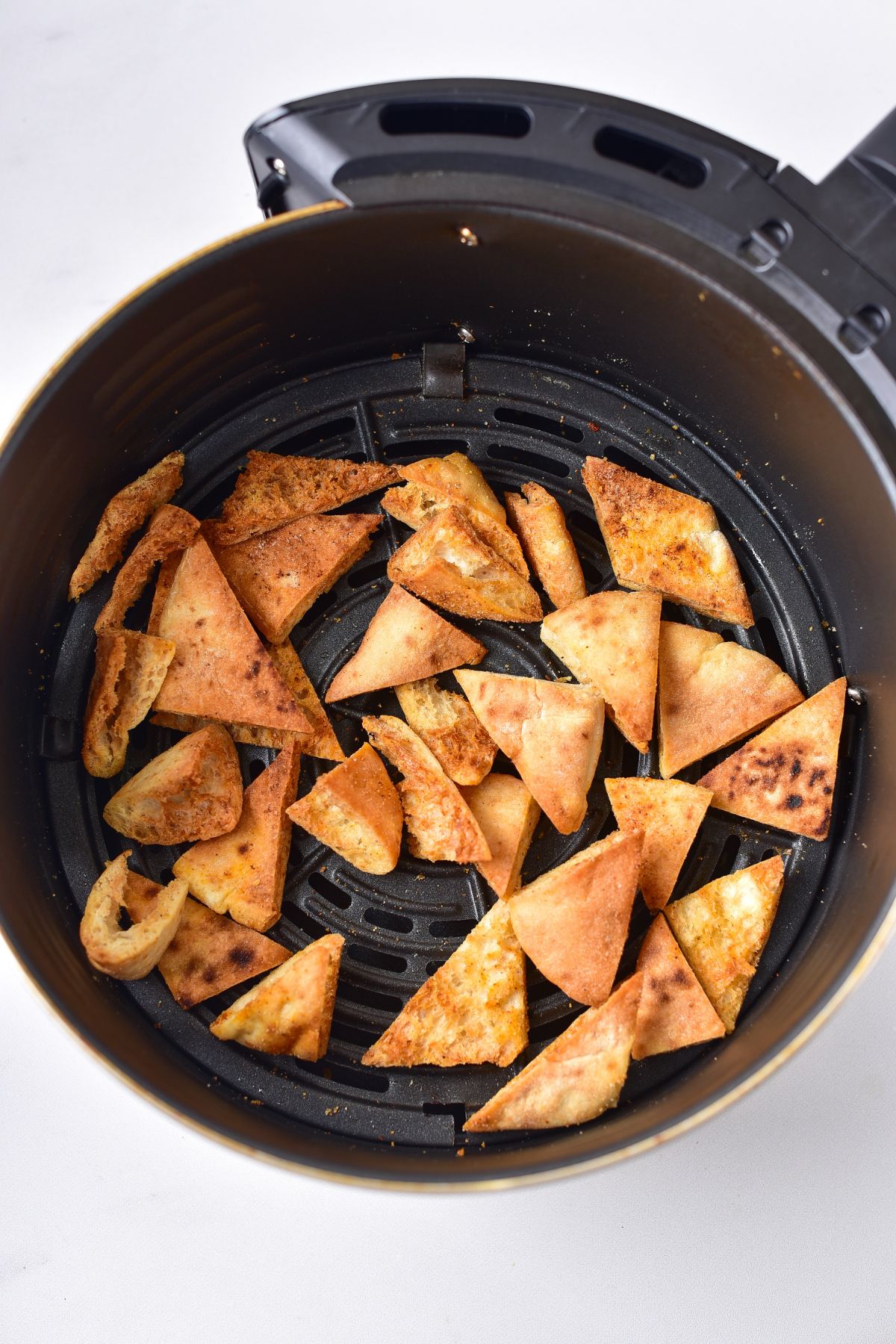 pita chips in an air fryer basket being toasted.