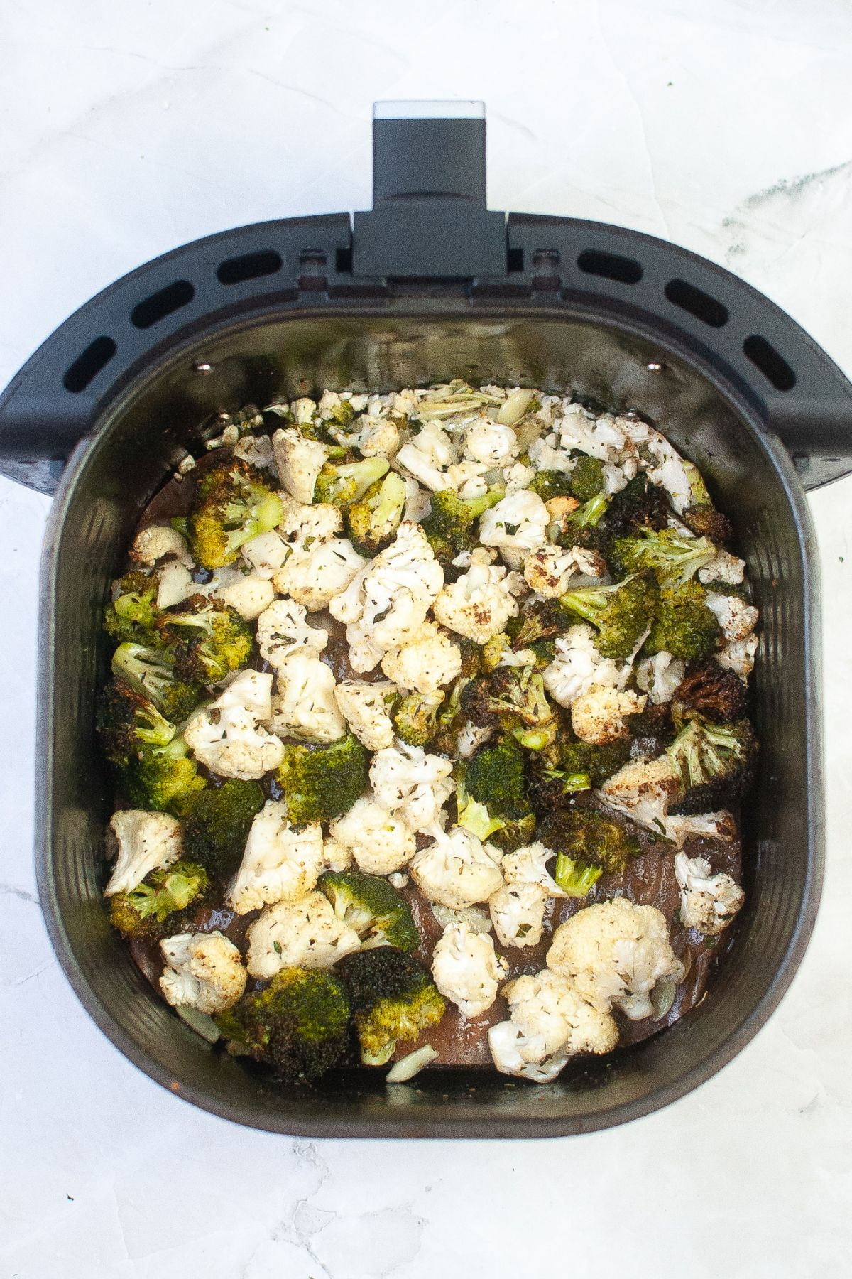broccoli and cauliflower being cooked in an air fryer basket.