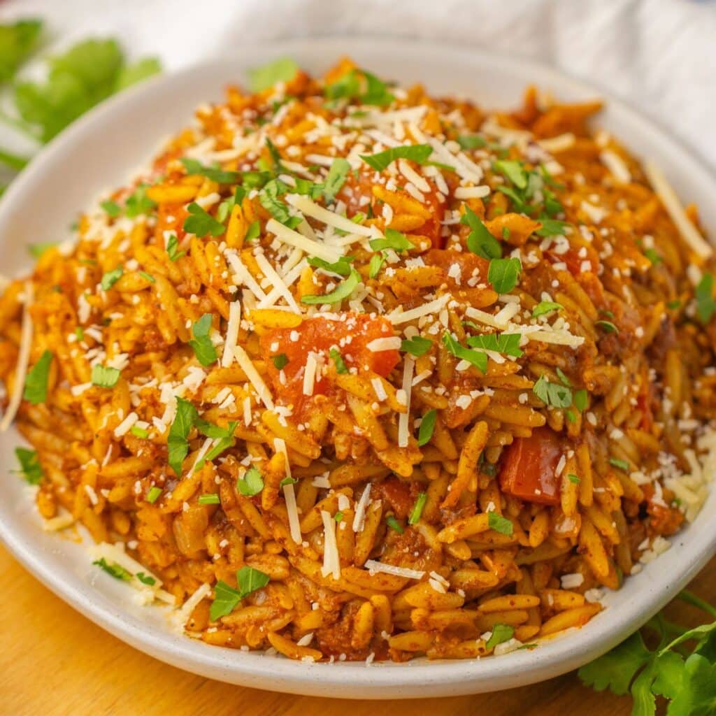 bowl full of cheesy chorizo orzo topped with parmesan and parsley.