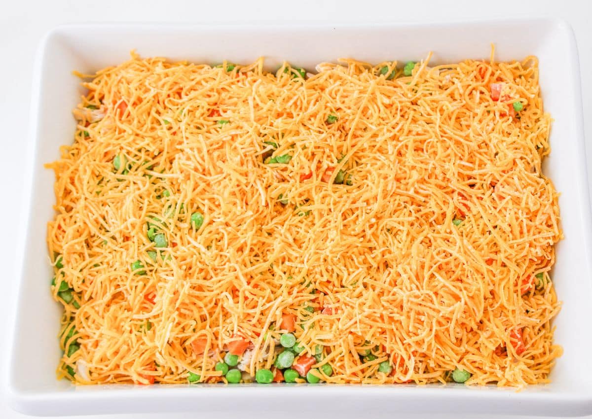 shredded cheese on top of peas and carrots in a casserole dish.