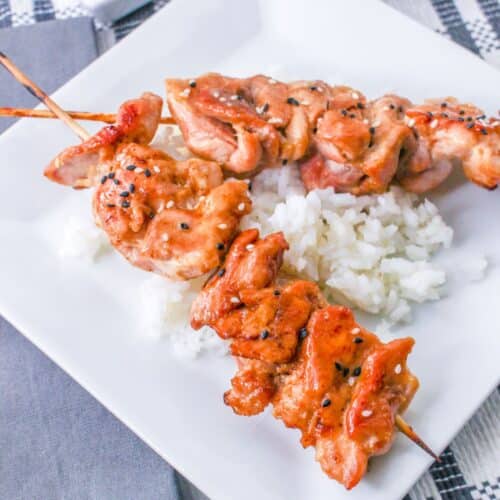 two chicken teriyaki on a stick skewers on a top of a bed of rice on a plate.