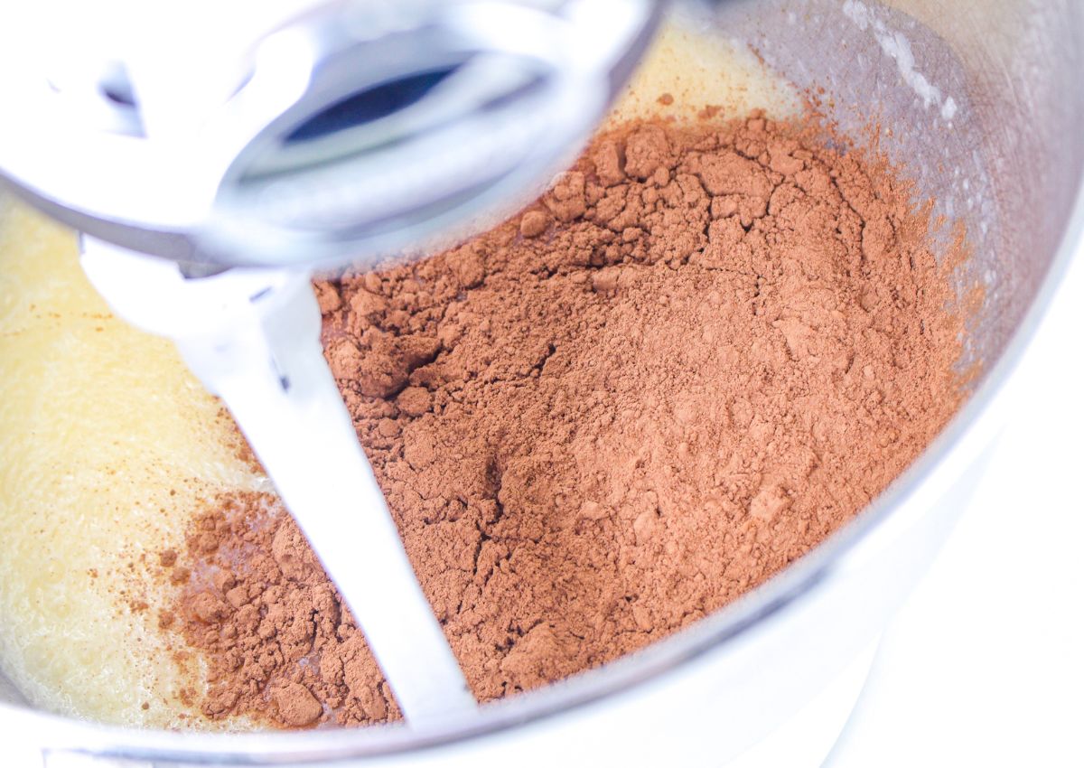 cocoa powder being added to batter in a stand mixer.