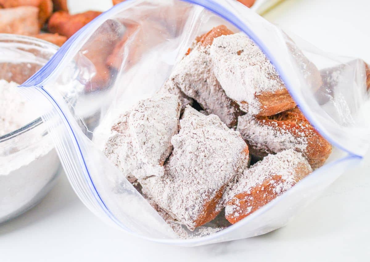 fried beignets being coated in powdered sugar in a large ziploc bag.