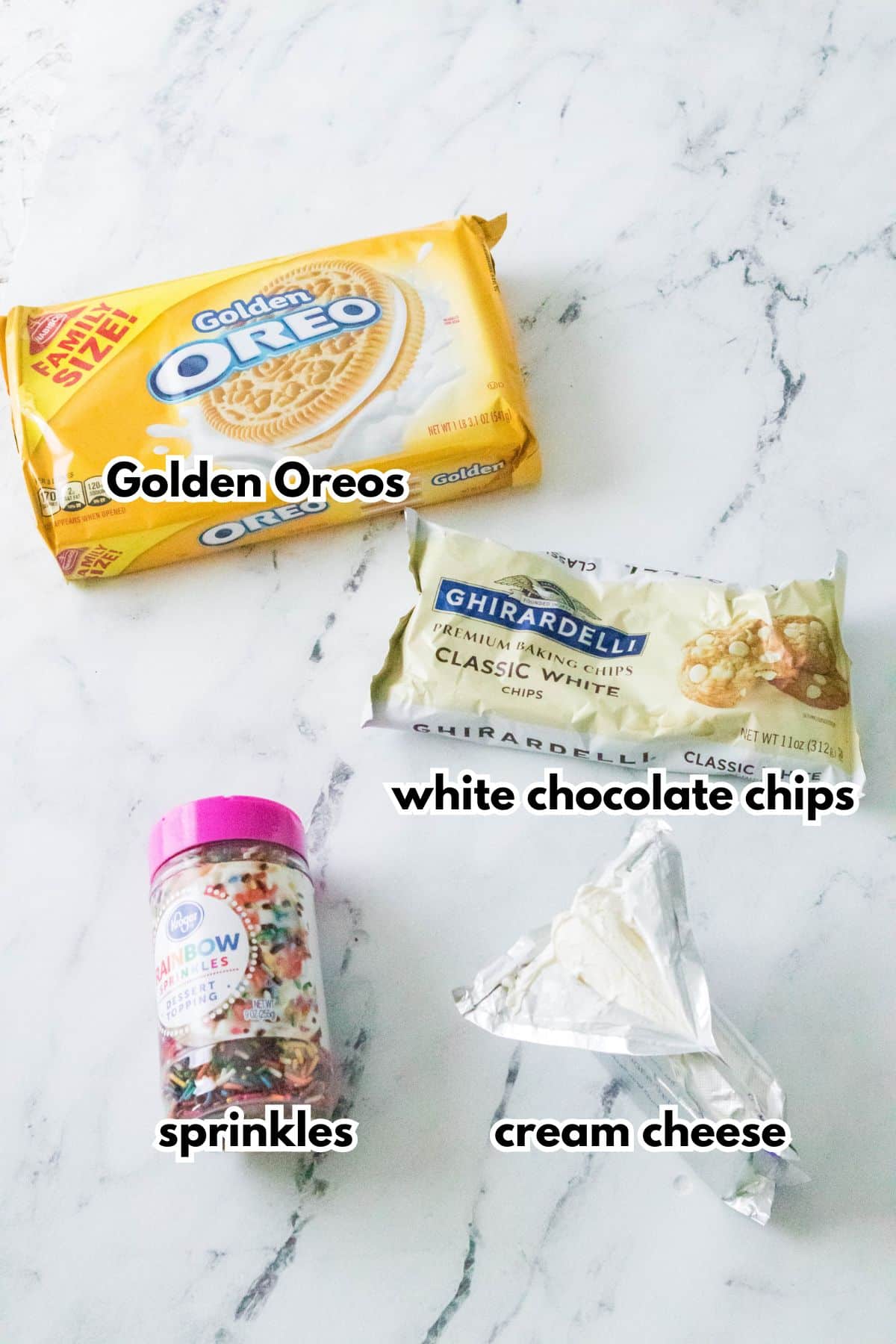 Oreos, sprinkles, cream cheese, and white chocolate on a marble counter.