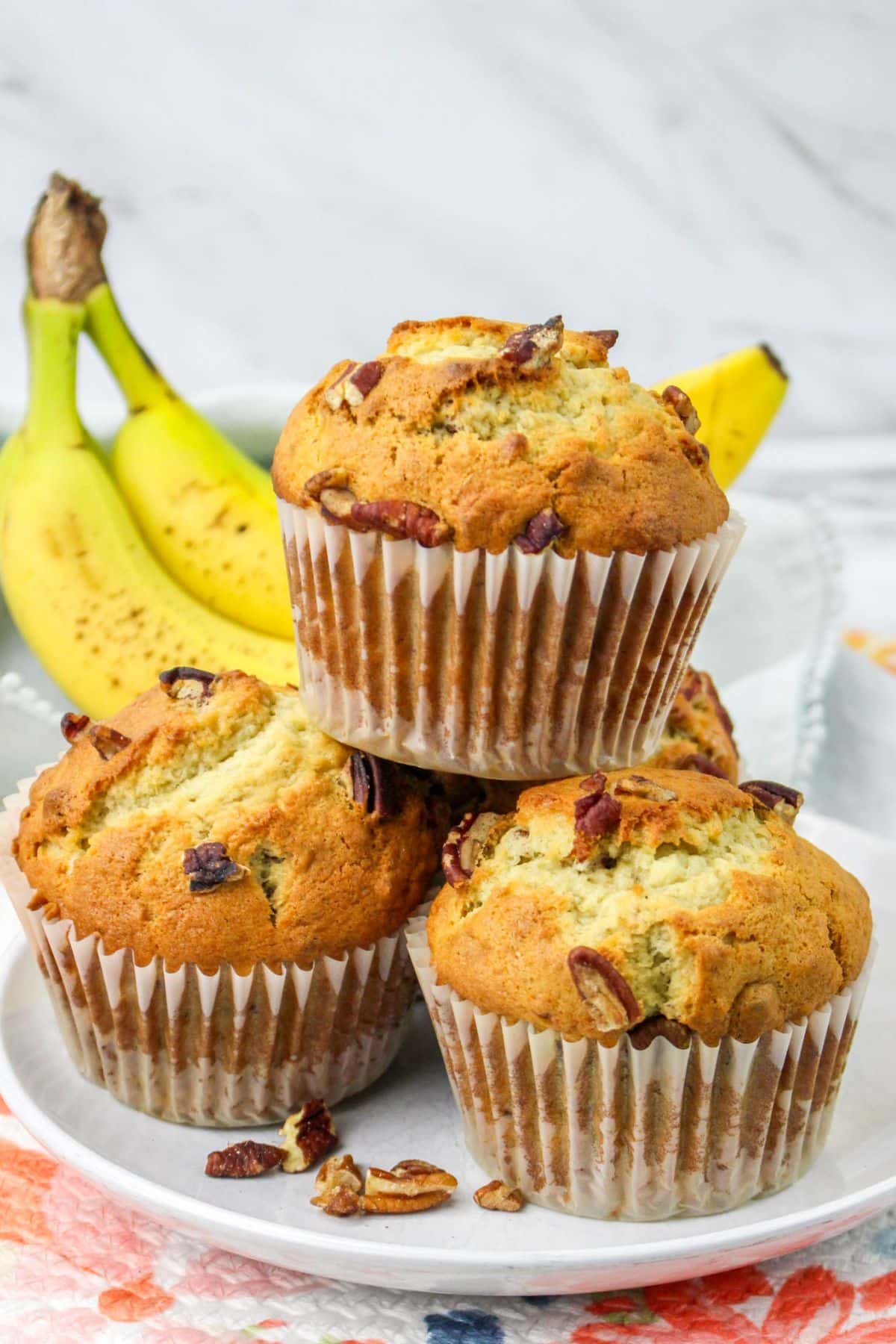 four jumbo banana nut muffins stacked in a pyramid on a plate.