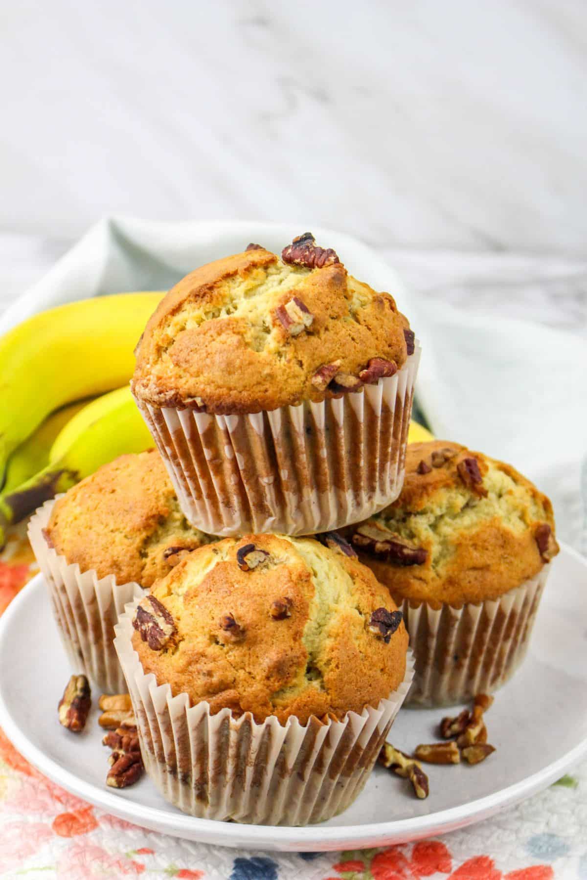 four jumbo banana nut muffins stacked in a pyramid on a plate.