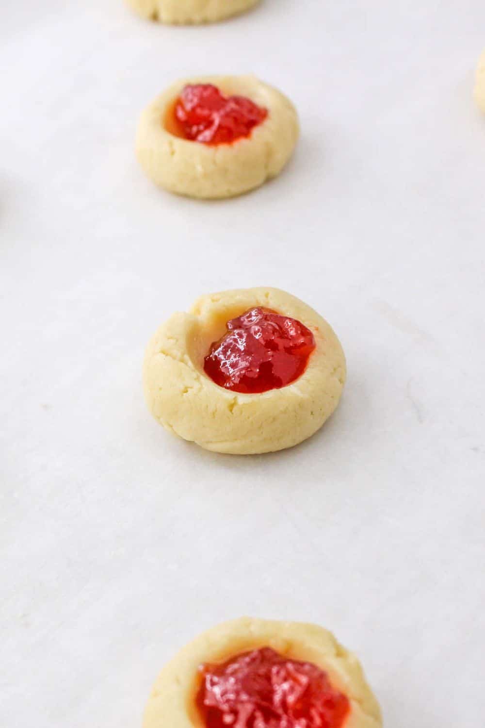 thumbprint cookies on a cookie sheet with a fruit jam in the center of the raw cookie dough