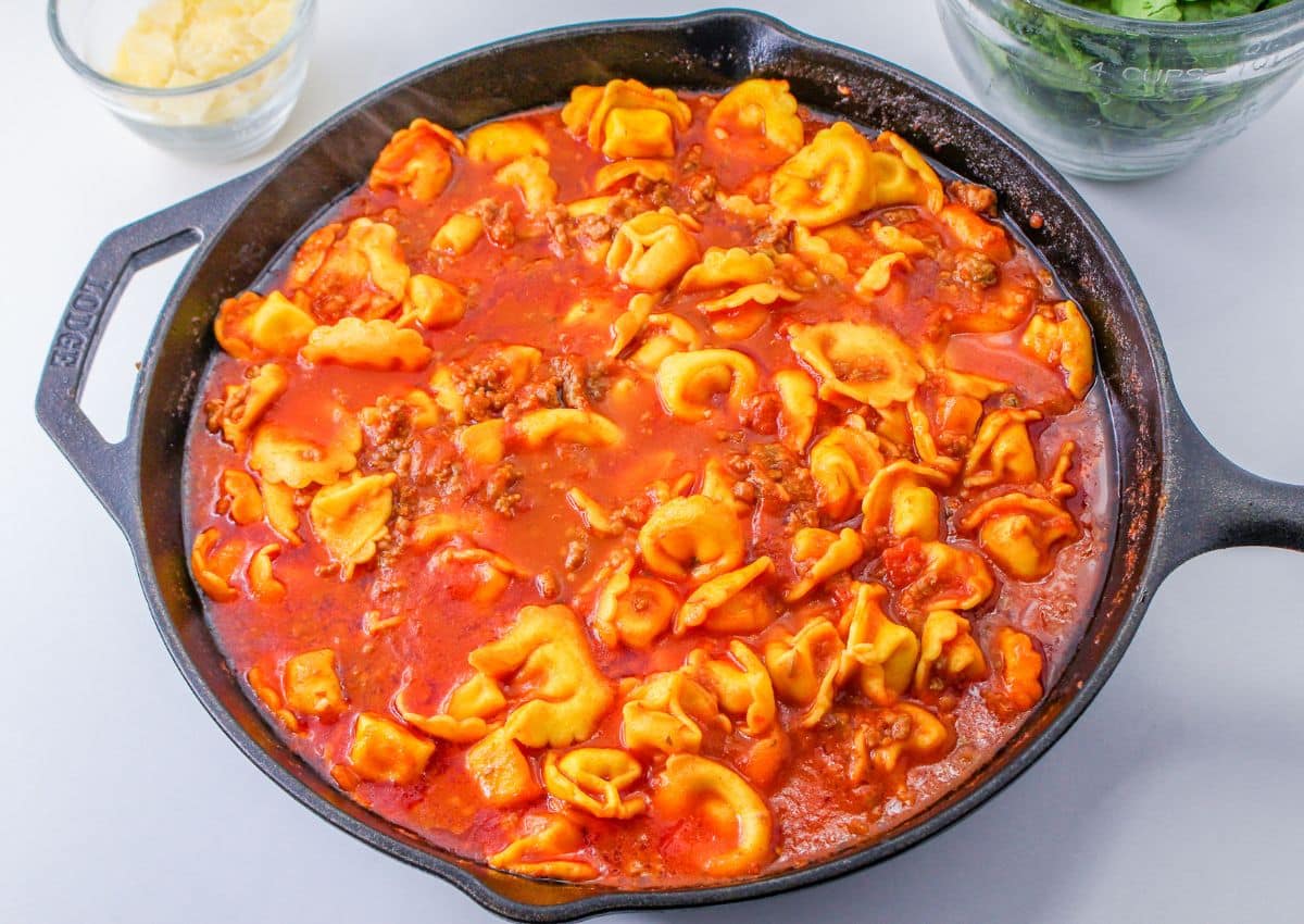 tortellini being cooked in tomato sauce and broth in a cast iron skillet.