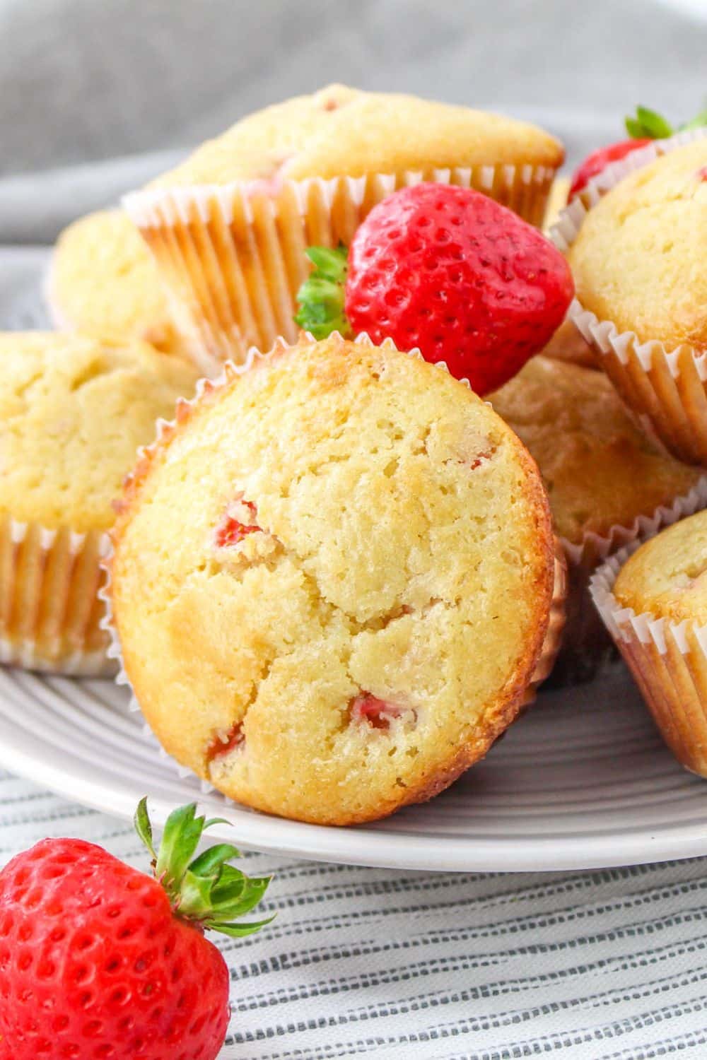 close up of strawberry muffins on plate with a few fresh berries around muffins
