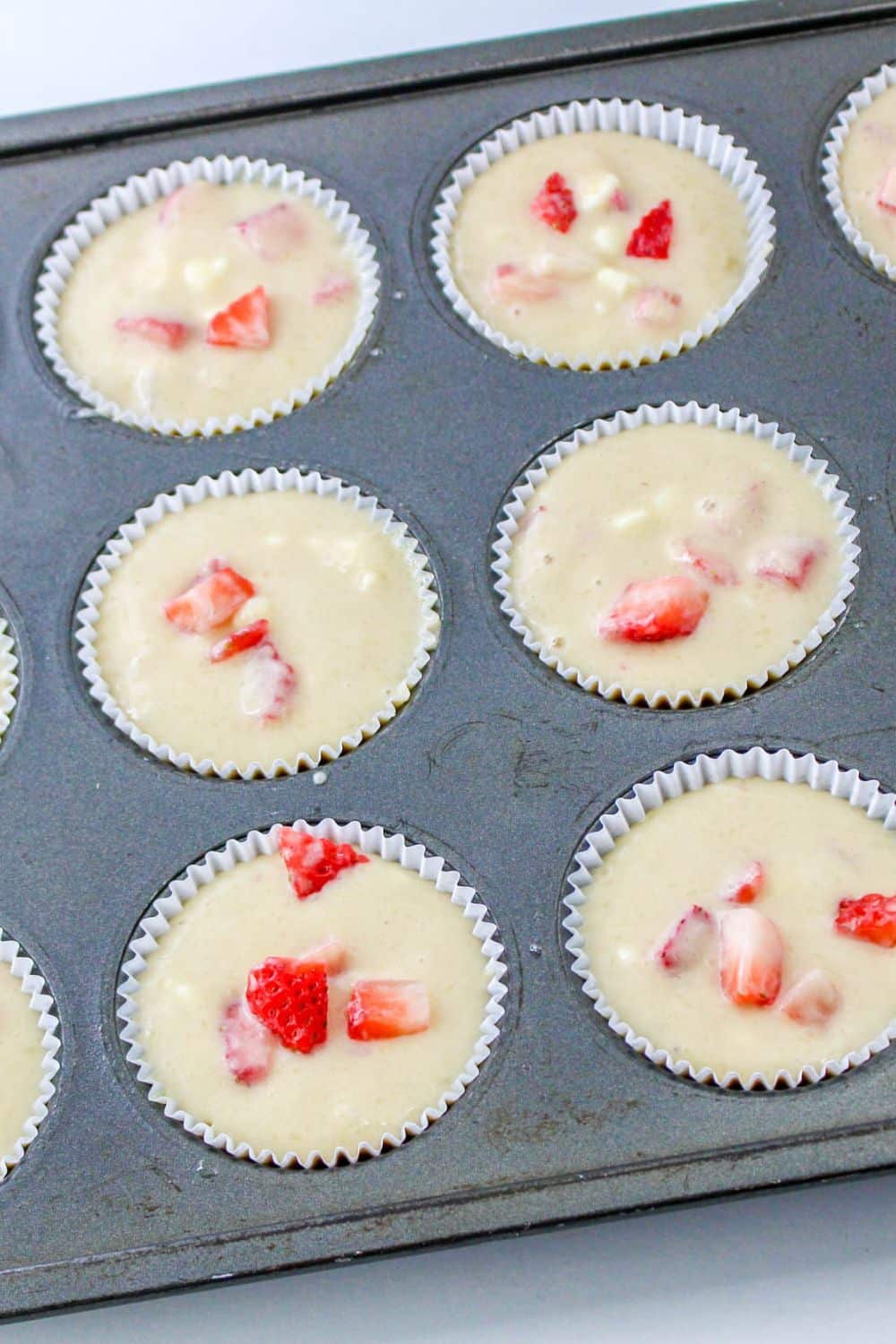 Strawberry White Chocolate Chip Muffins in a muffin tin that are wet batter, uncooked