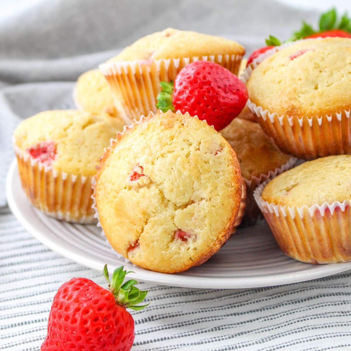 Strawberry White Chocolate Chip Muffins on a plate with a few fresh berries around the plate