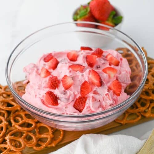 strawberry pretzel dip in a glass bowl and topped with sliced fresh strawberries.