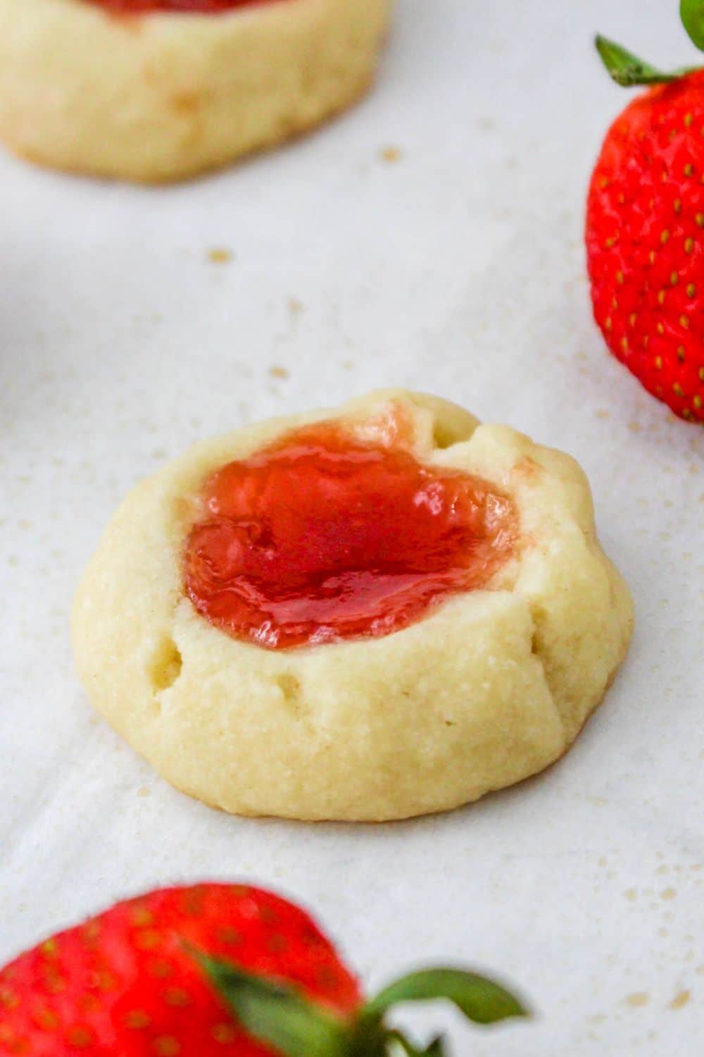 thumbprint cookies on a parchment paper lined pan with a few strawberries by cookies