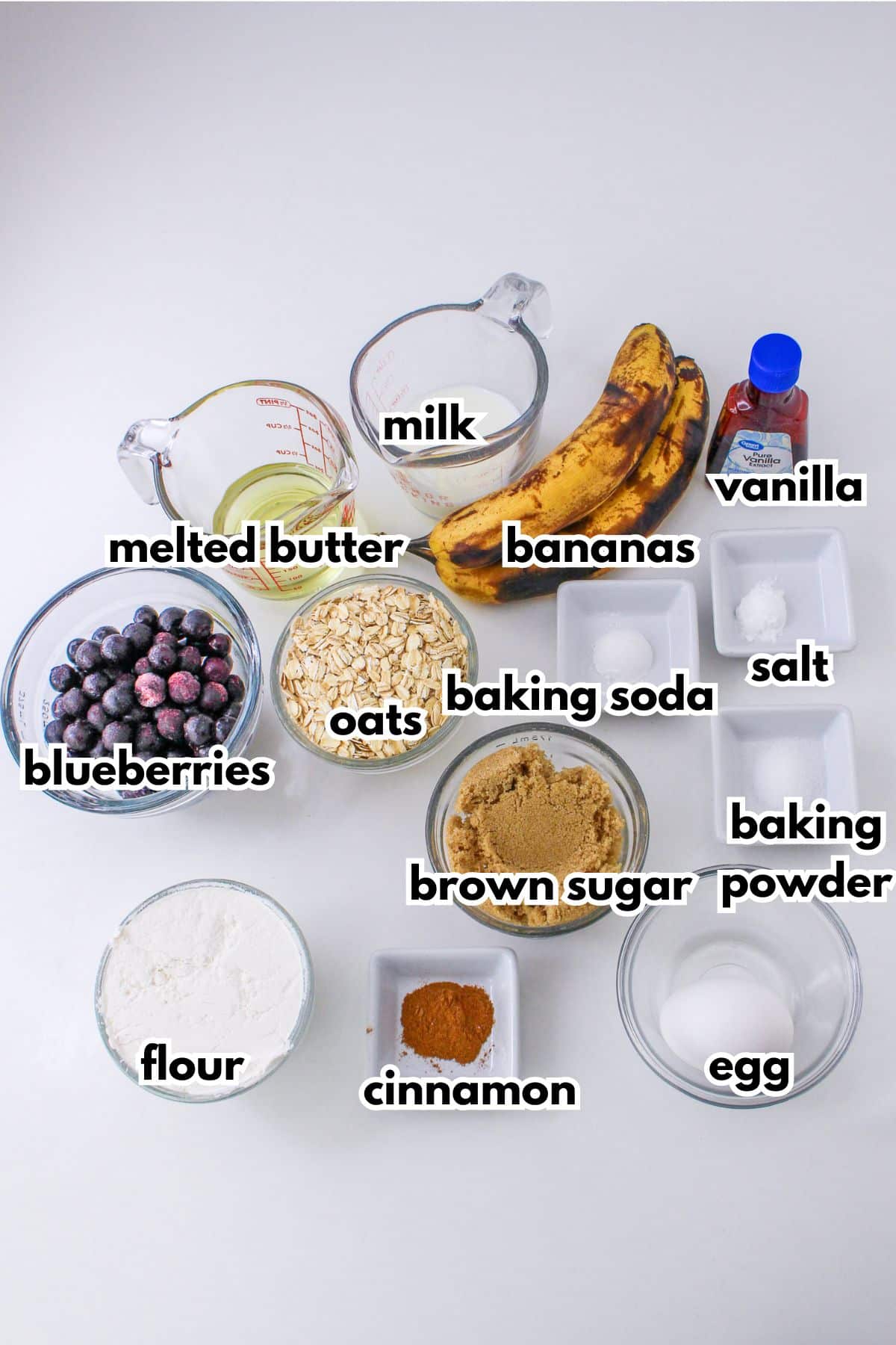 bowls of melted butter, milk, blueberries, oats, flour, cinnamon, brown sugar, baking soda, baking powder, salt, bananas and an egg.