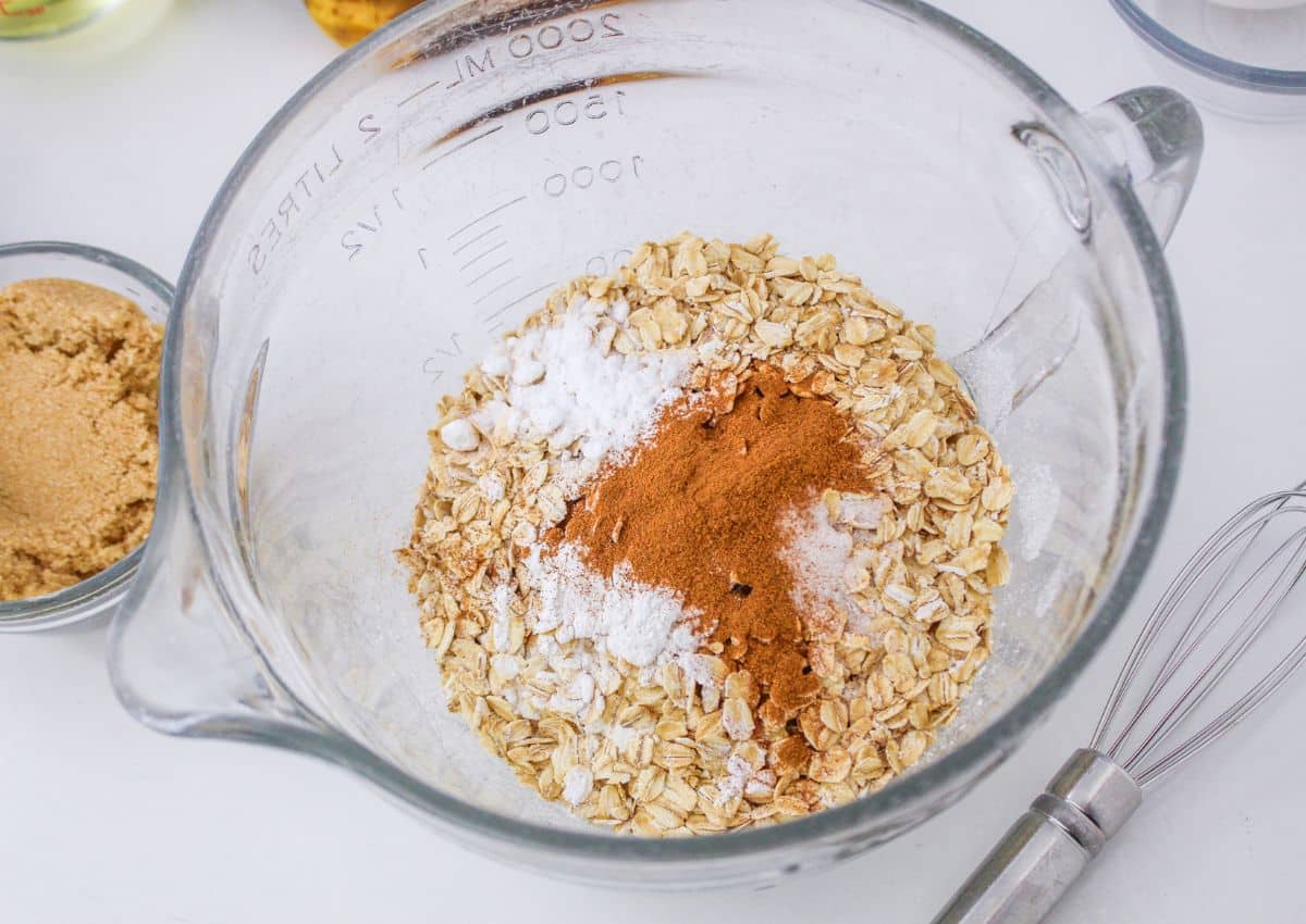 flour, oats, baking soda, baking powder, salt, and cinnamon being mixed in a large glass mixing bowl.