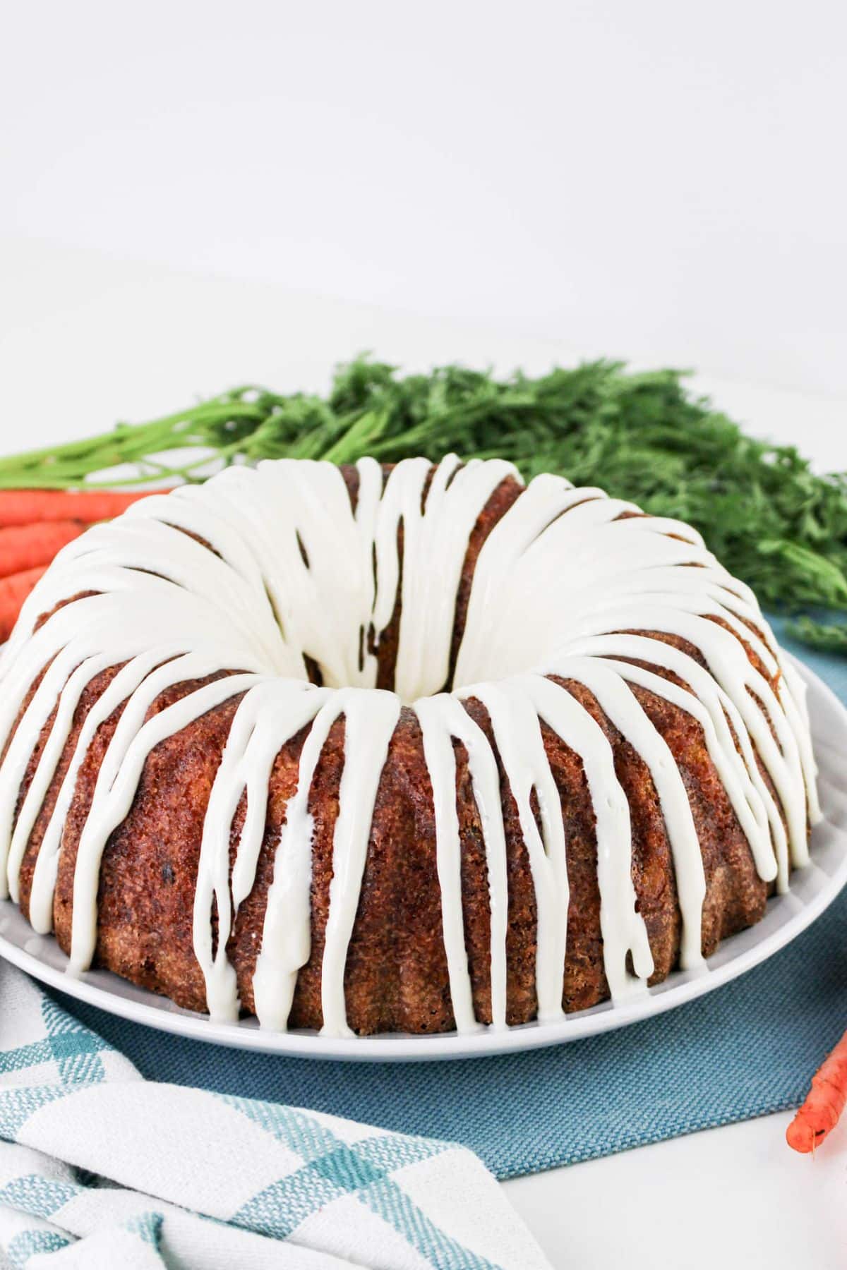 uncut carrot pound cake topped with cream cheese frosting on a plate.