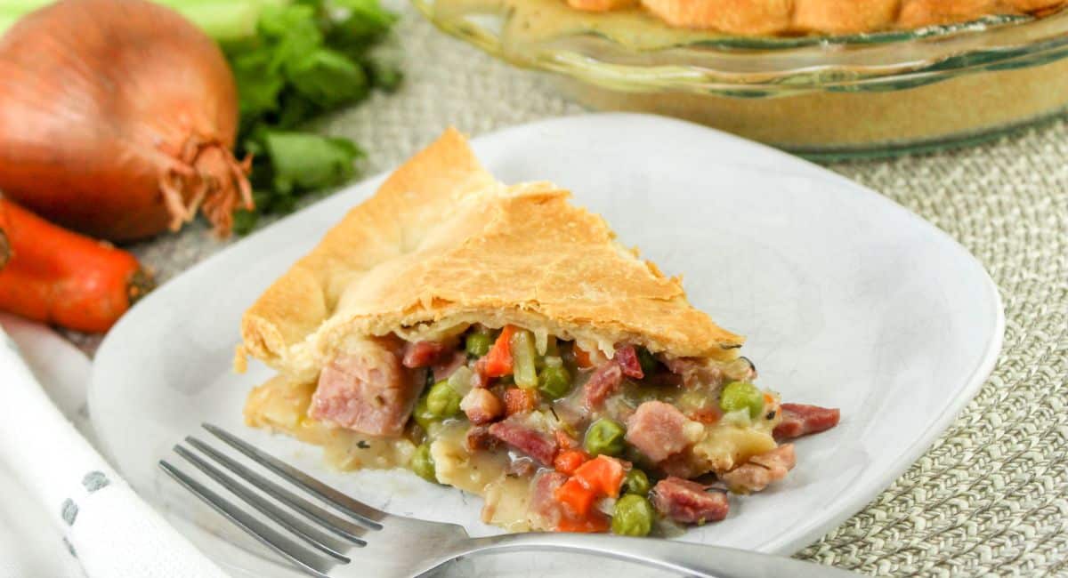 slice of ham pot pie on a plate with a fork next to it.