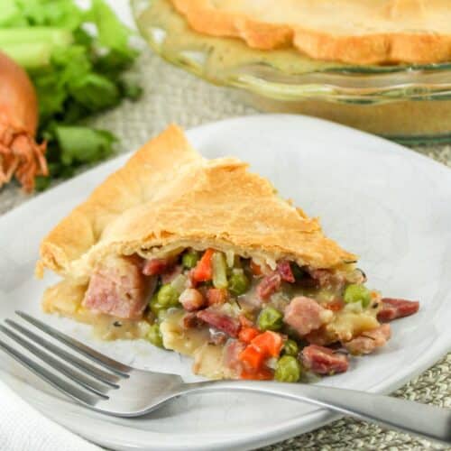 slice of ham pot pie on a plate with a fork next to it.