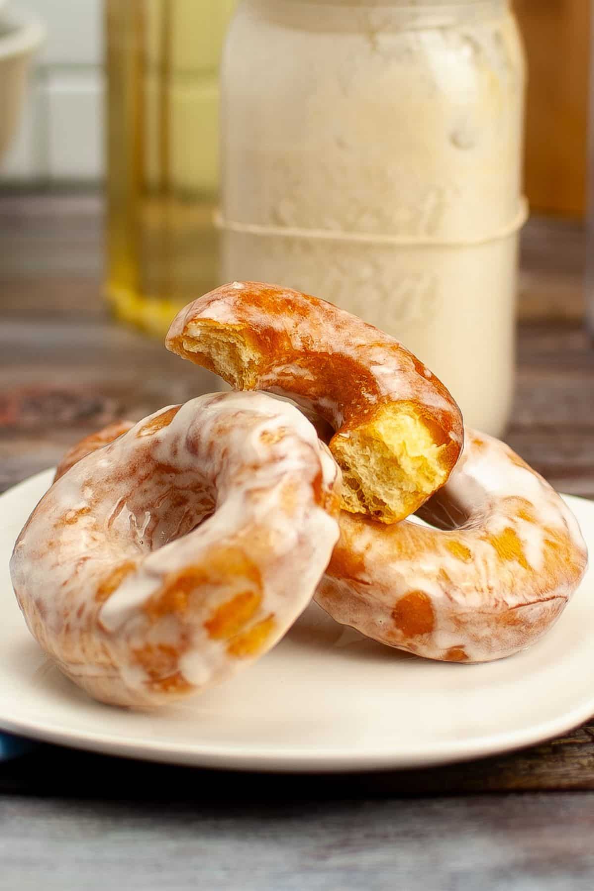 four glazed sourdough donuts stacked on a plate with the top one broken in half.