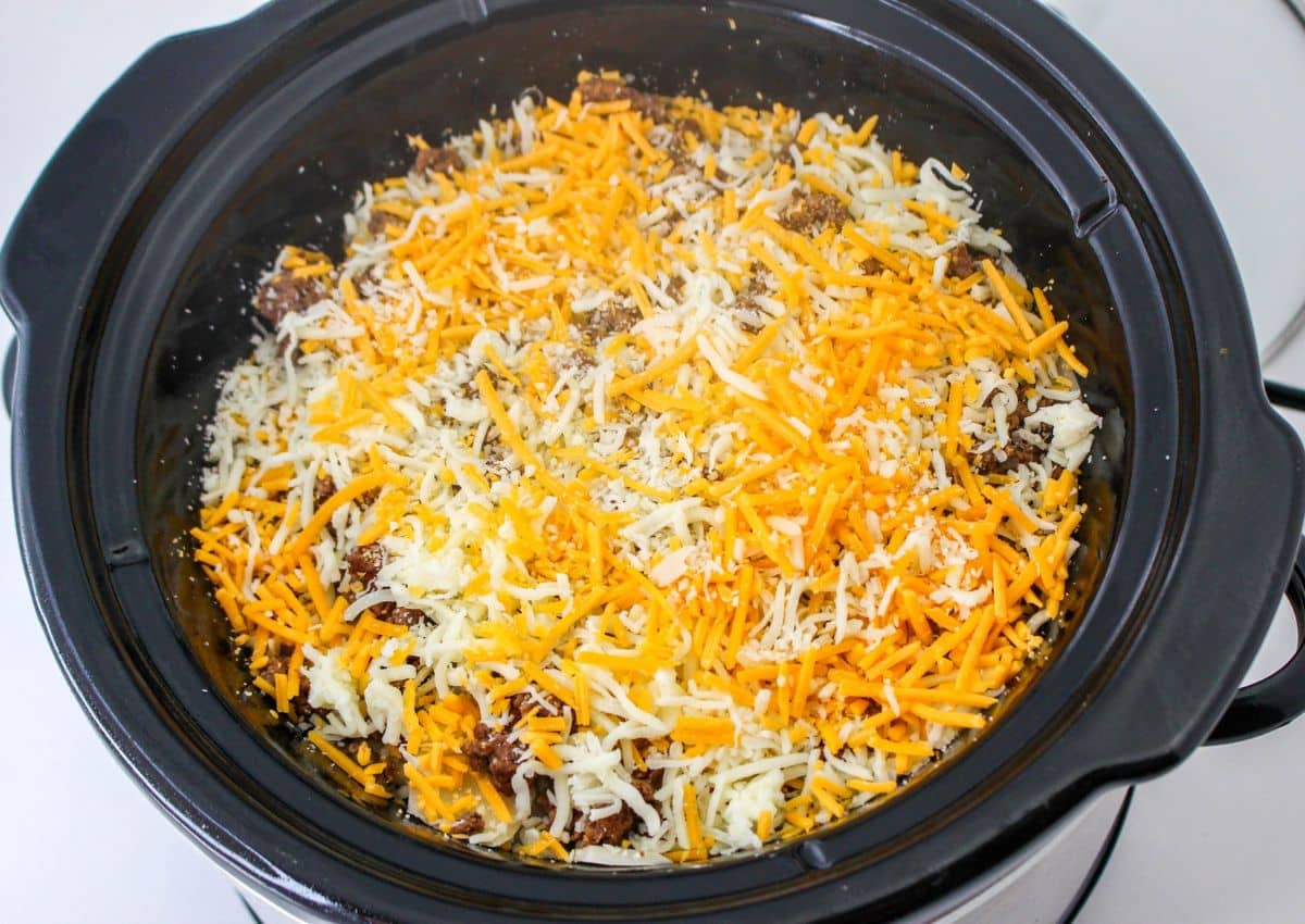 cheese being added to the tops of potatoes and beef in a slow cooker.