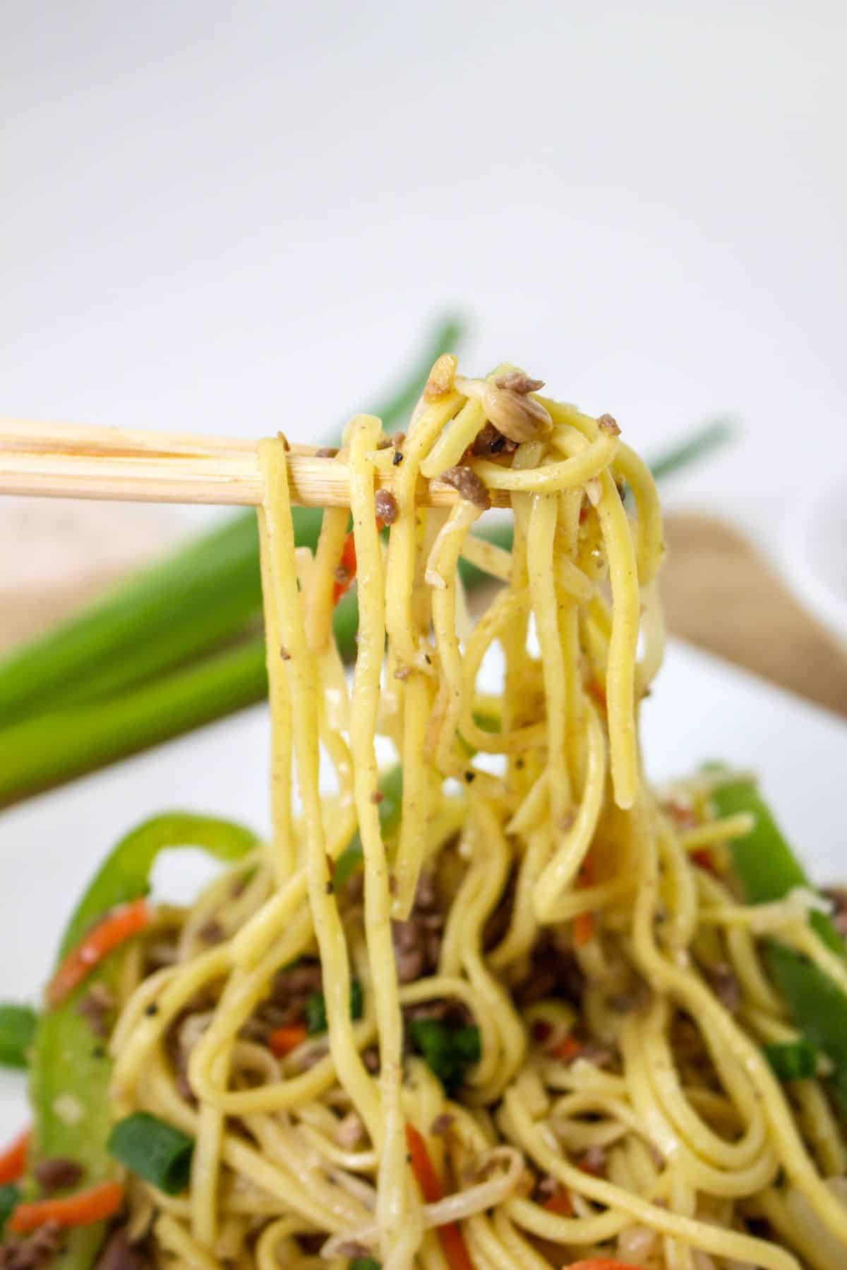 chow mein noodles held in the air on a chop sticks.