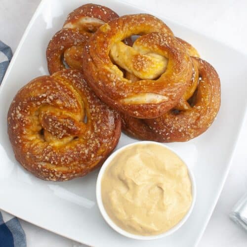 five sourdough soft pretzels stacked on a plate.