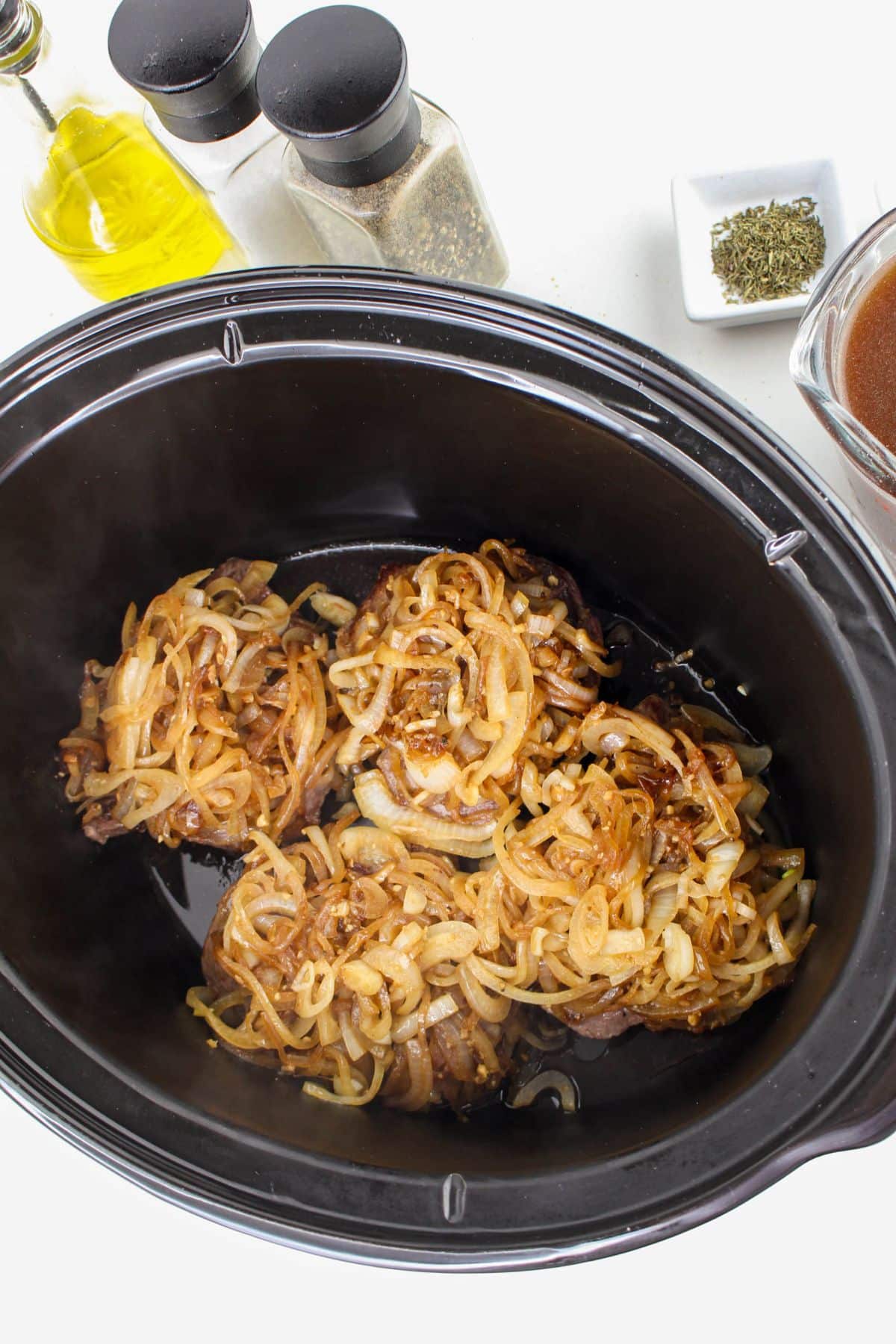 caramelized onions being putting on top of steak in a slow cooker.