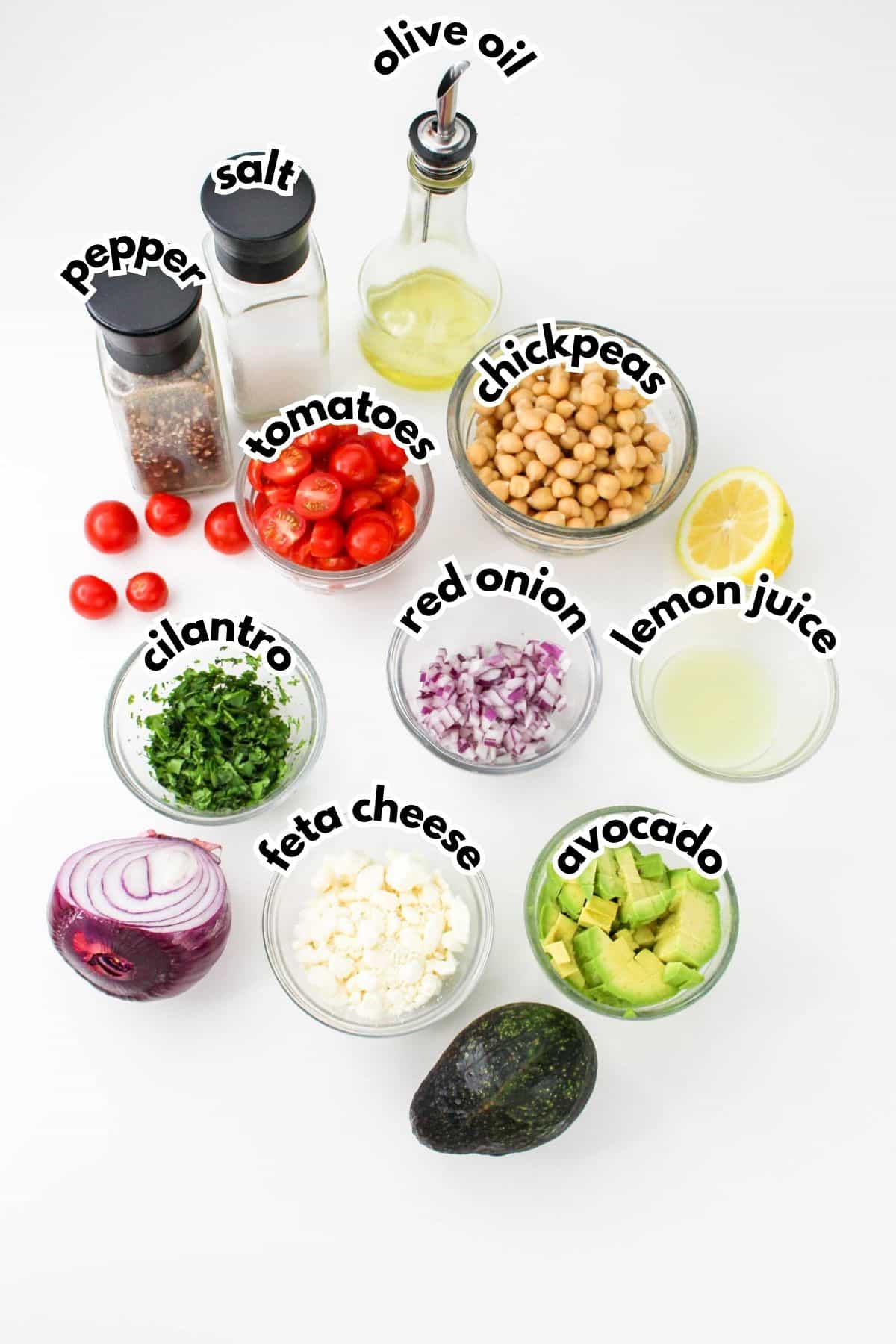 bowls of salt, pepper,olive oil, tomatoes, chickpeas, cilantro, red onion, lemon juice, feta cheese, and avocado on a counter.