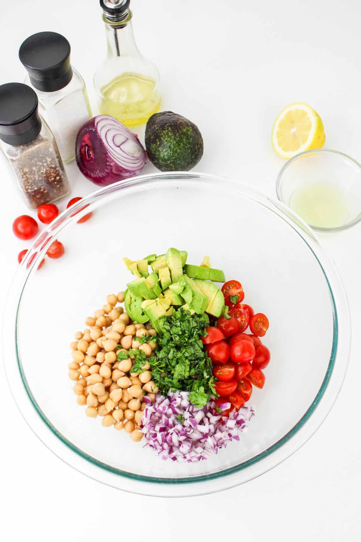 avocados, chickpeas, tomatoes, red onion, and cliantro in a glass bowl.