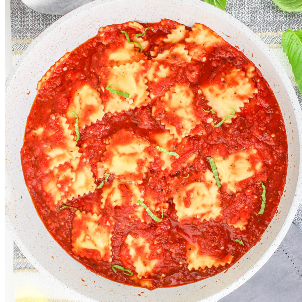 A pan filled with square ravioli pomodoro in tomato sauce, garnished with fresh basil leaves.