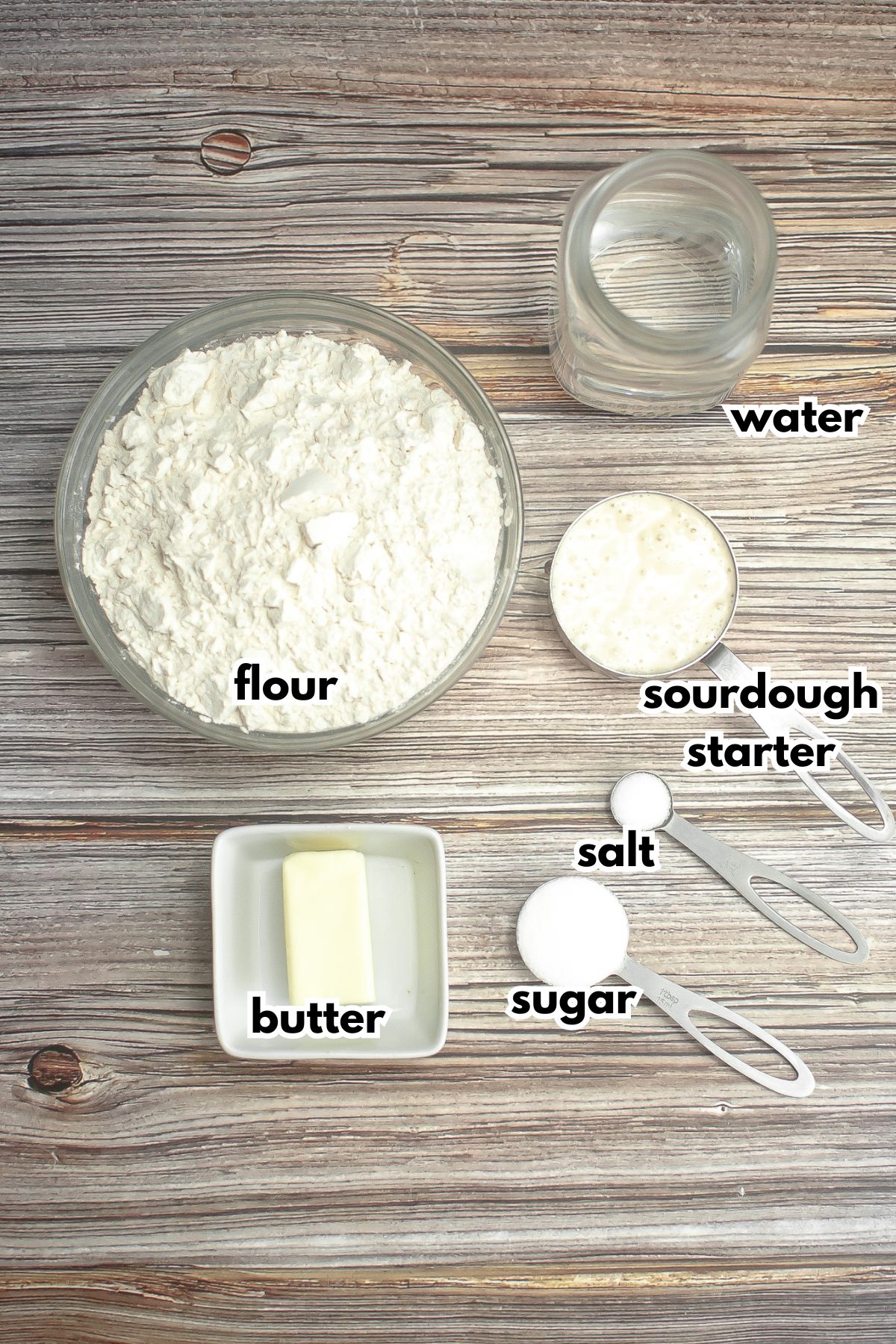 bowls of flour, water, sourdough starter, salt, sugar, and butter on a counter.