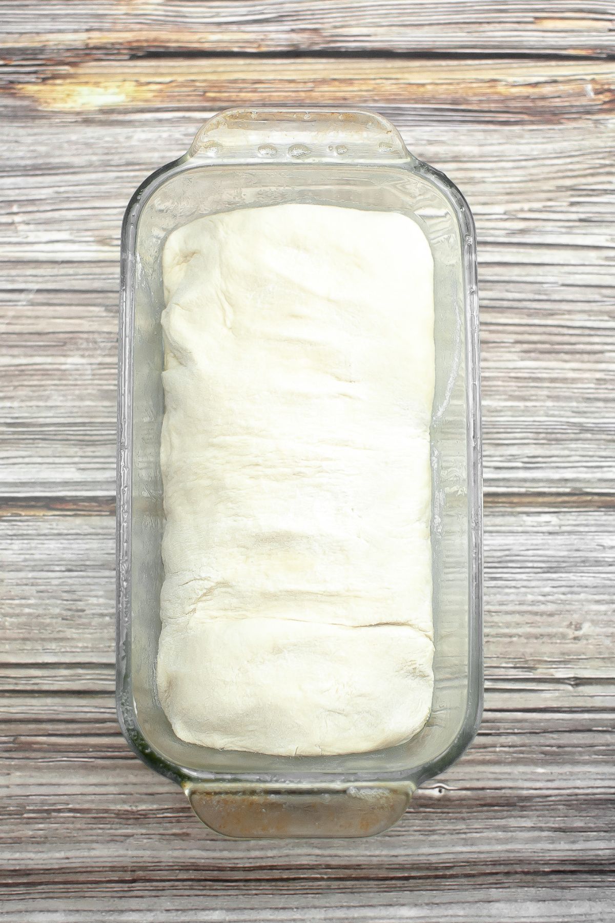 raw sourdough loaf in a glass loaf pan.