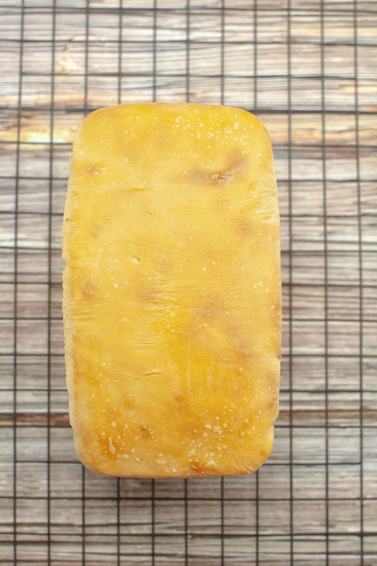 uncut loaf of sourdough sandwich bread on a cooling rack.