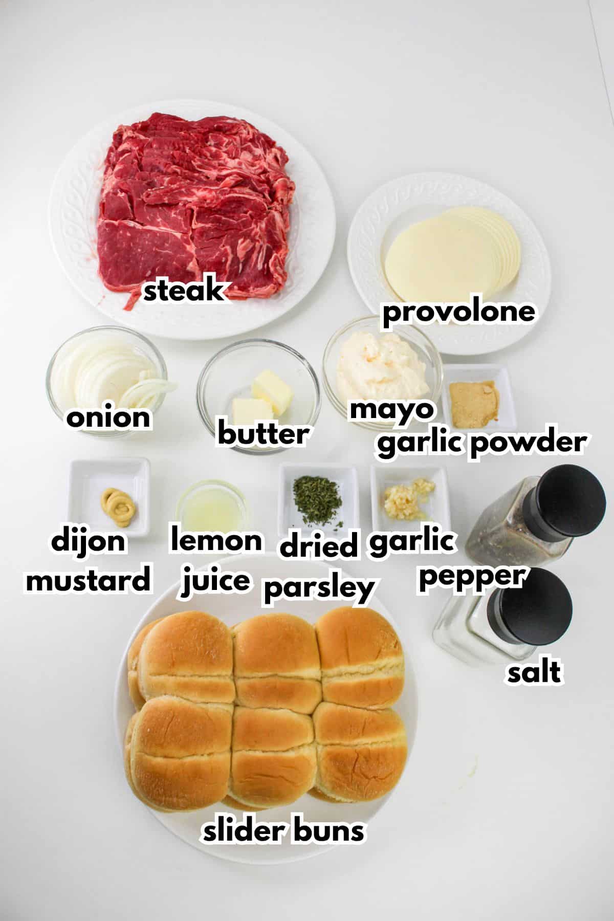 bowls of steak, provolone, onion, butter, mayo, garlic powder, dijon mustard, lemon juice, dried parsley, garlic, pepper, salt, and slider buns on a counter.