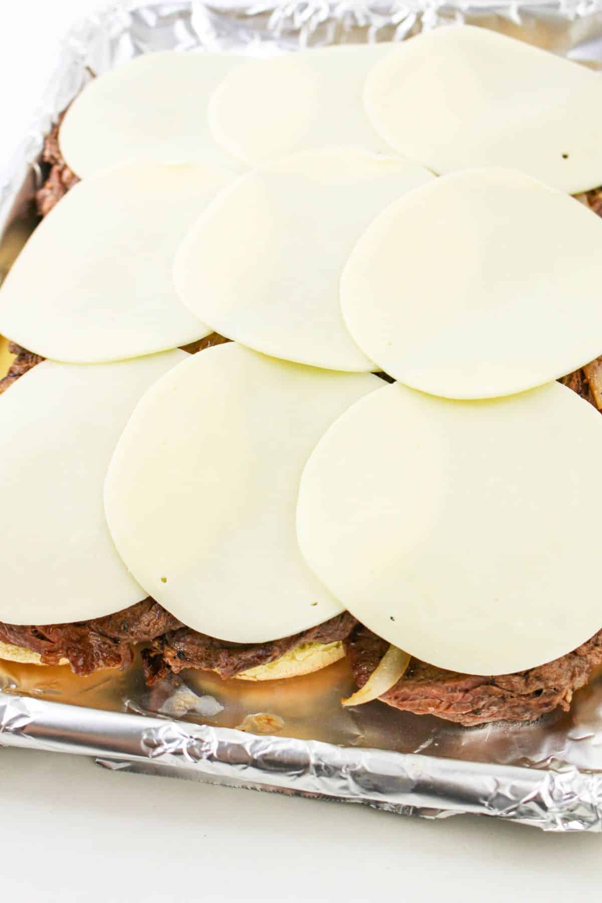 cheese being laid on top of steaks on a baking sheet.