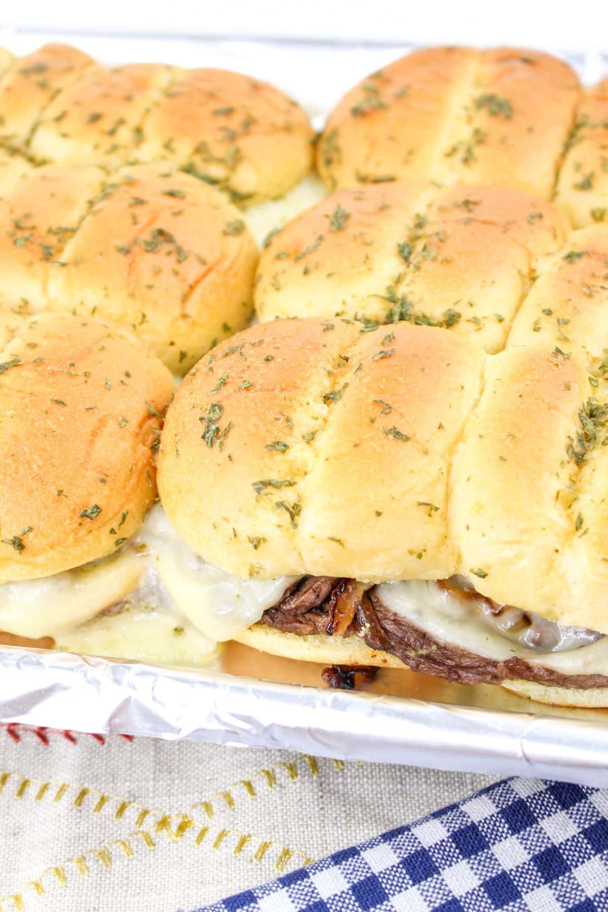 finished steak and cheese sliders on a baking dish.