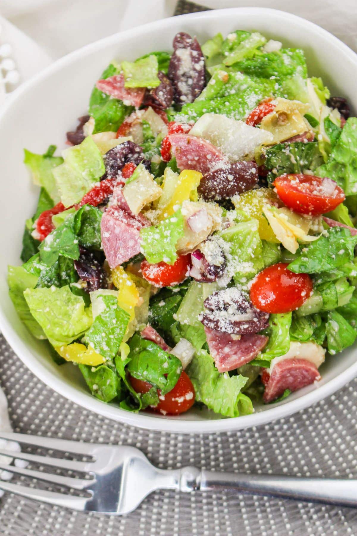 bowl filled with lettuce, tomatoes, olives, salami and dressing.