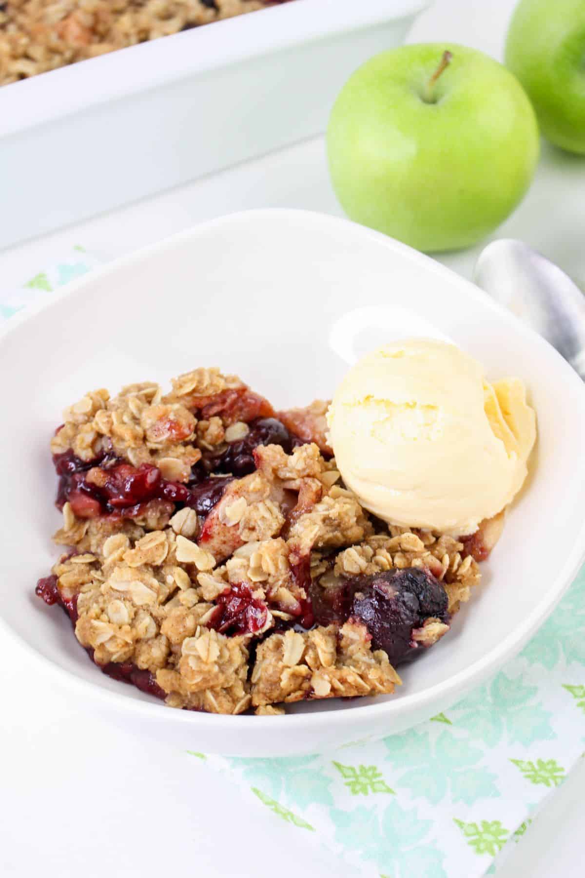 bowl of cherry apple crisp topped with vanilla ice cream on a table.