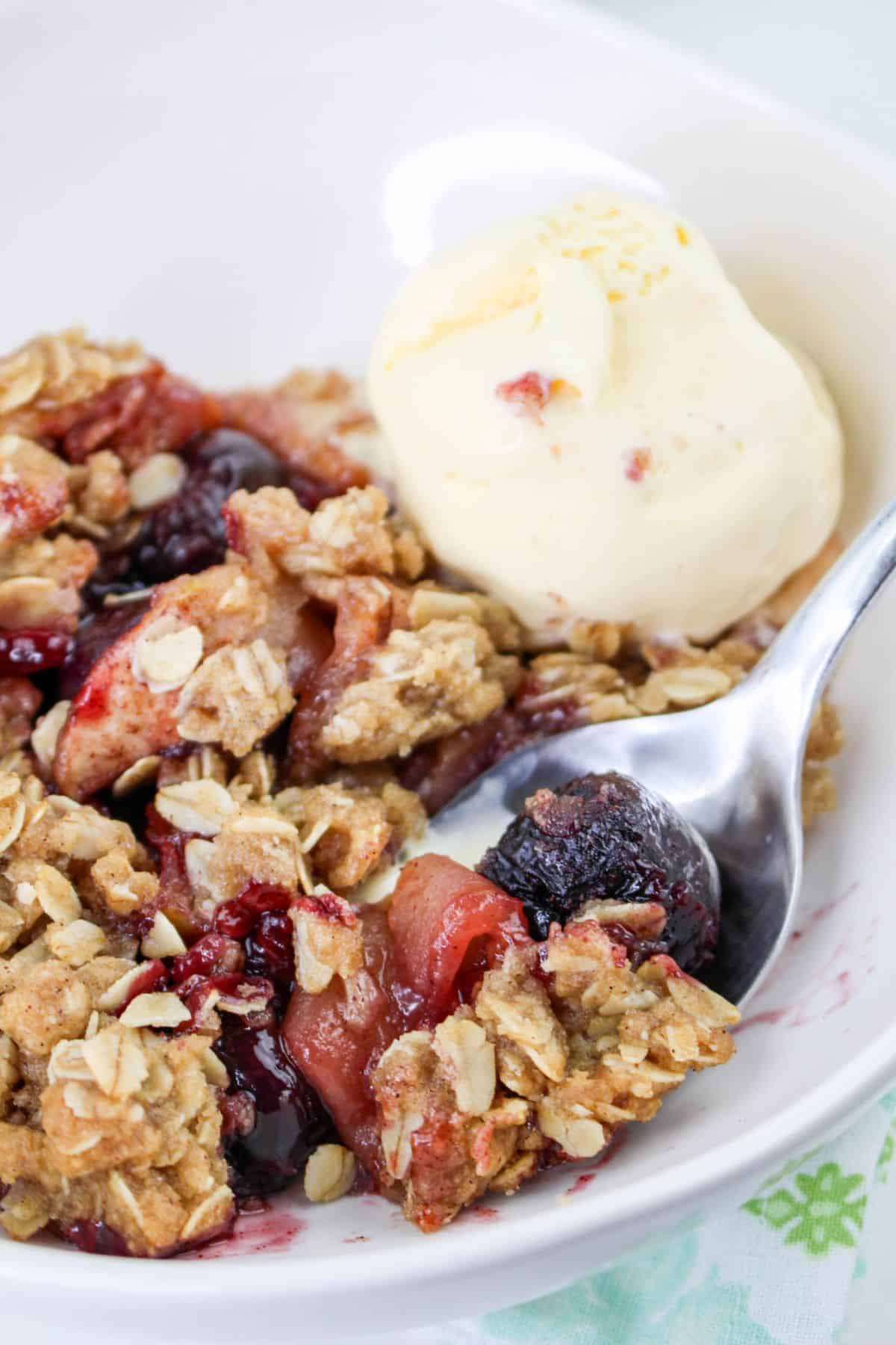 bowl of cherry apple crisp topped with vanilla ice cream on a table.