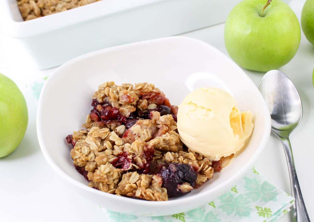 bowl of cherry apple crisp topped with vanilla ice cream on a table.