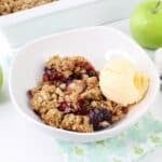 bowl of cherry apple crisp topped with vanilla ice cream on a table.