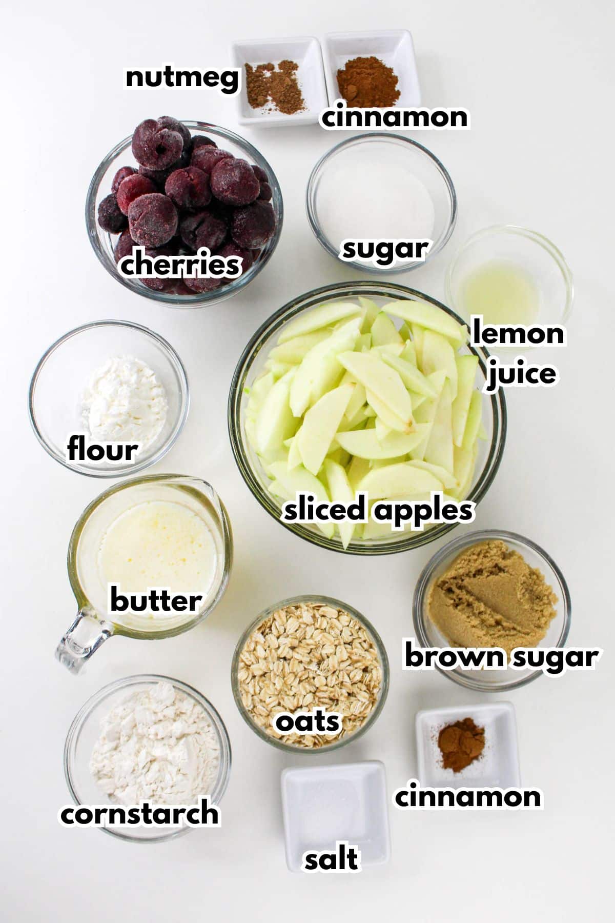 bowls of nutmeg,cinnamon,cherries, sugar, flour, butter, apples, lemon juice, cornstarch, oats, brown sugar, and salt on a counter.