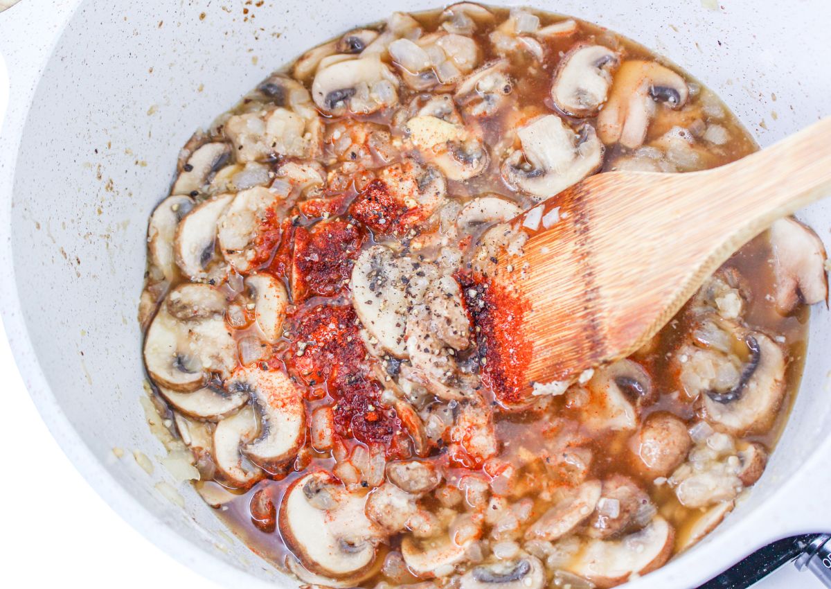 paprika, salt, and pepper being added to a pot of cooked mushrooms and onions.