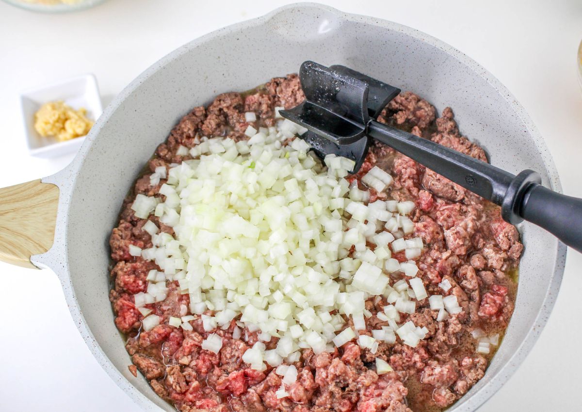 onions and ground beef being cooked in a large skillet.